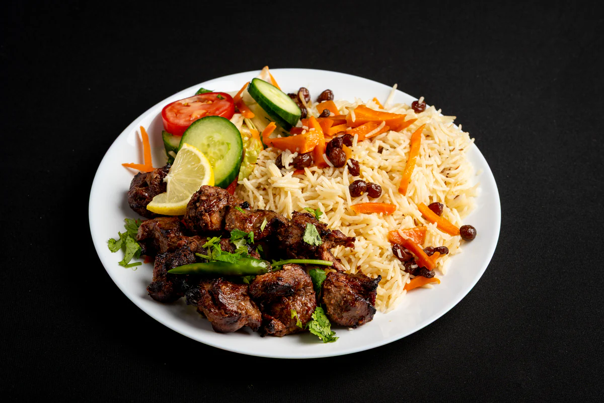 Charred beef tikka piled beside pulao rice, with cucumber, tomato, lemon and a green chilli.