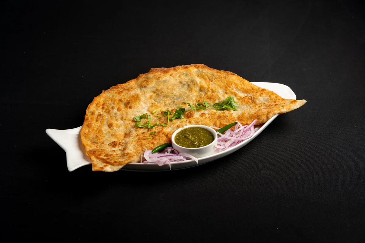 A folded bolani, blistered and golden, on a white plate with green chutney and sliced red onion.