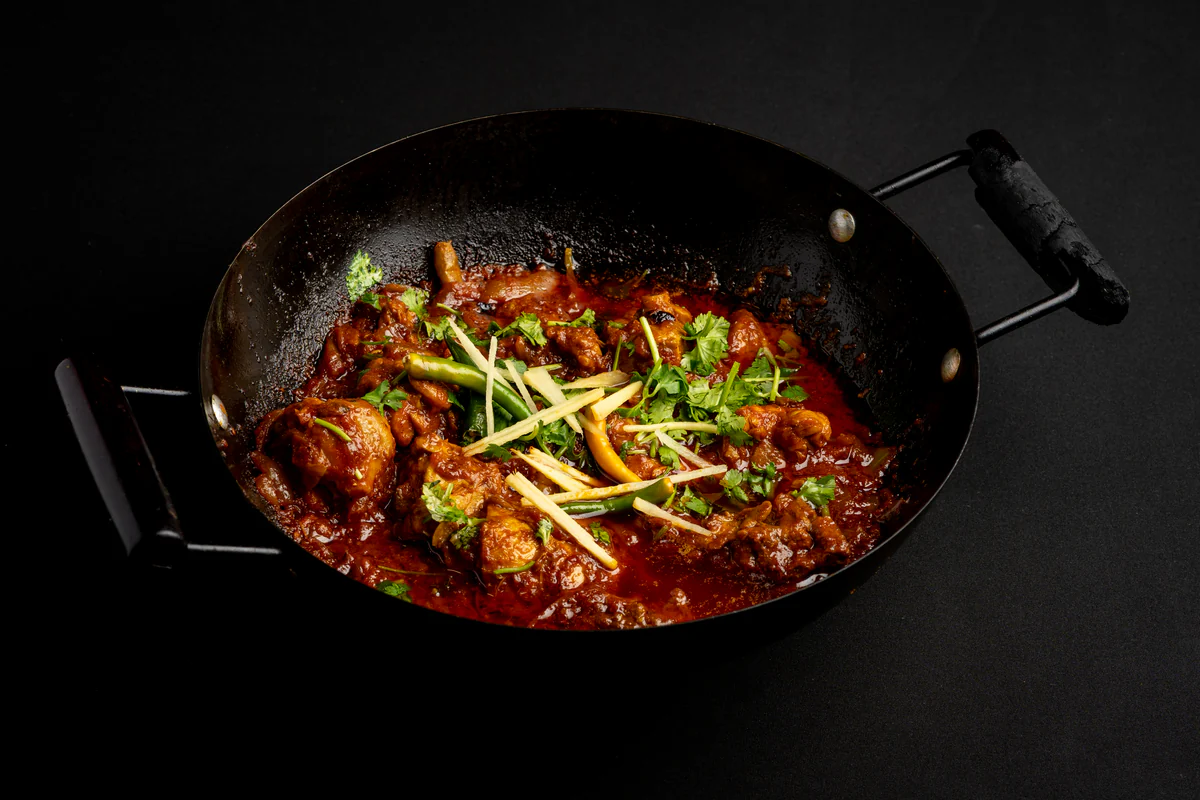 Chicken curry in a black karahi, pieces on the bone in a deep red sauce with ginger, coriander and green chilli.