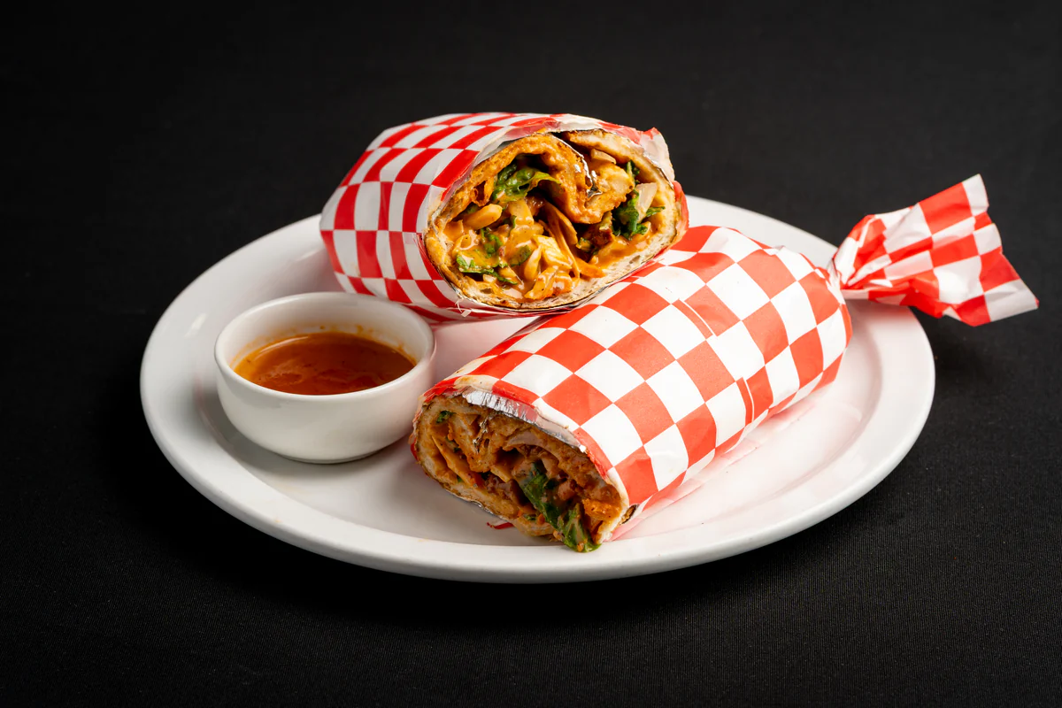 A chicken wrap cut in two and stood on a white plate in red checked paper, showing the chicken, fries and salad inside.