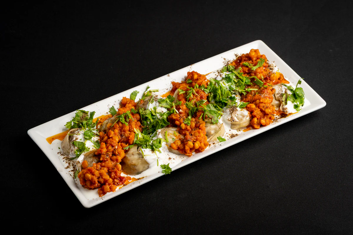 Manto dumplings on a long white plate under yogurt, split-pea sauce, coriander and dried mint.