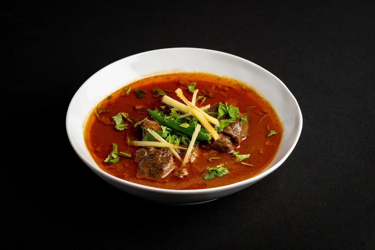 Beef nihari in a white bowl, dark stew under julienned ginger, coriander and a green chilli.