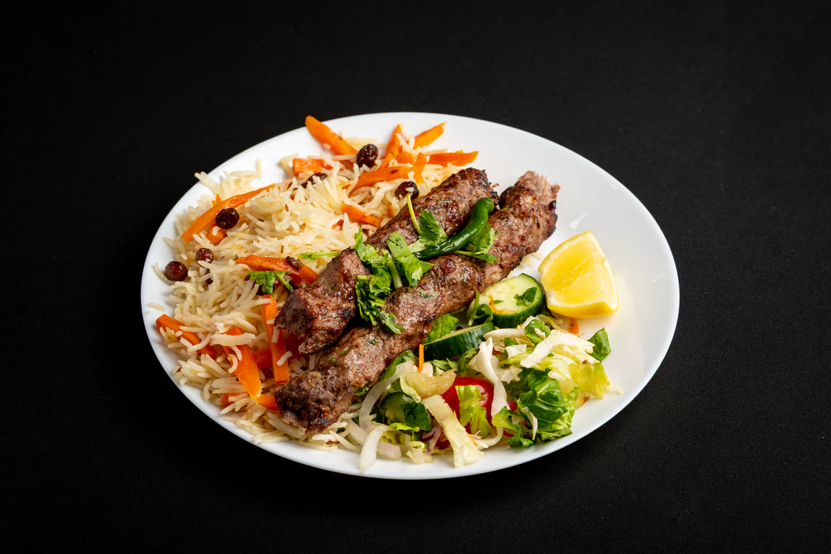 Two minced-beef sekh kabobs off the skewer, laid over pulao rice with shredded salad and a lemon wedge.